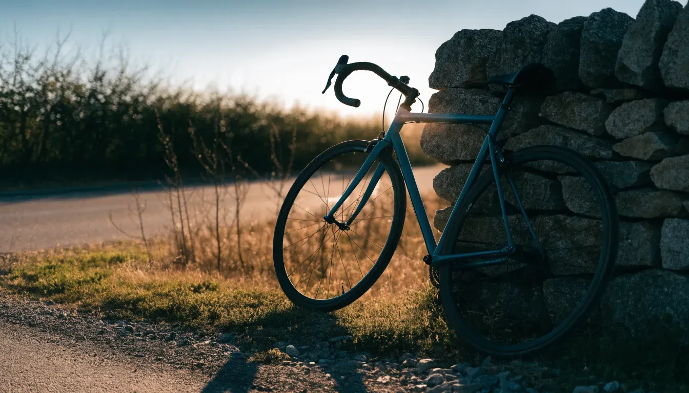 Ein Rennrad lehnt an einer Steinmauer am Straßenrand, die Sonne steht tief und wirft einen langen Schatten.